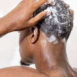 man washing hair in shower with zenore shampoo